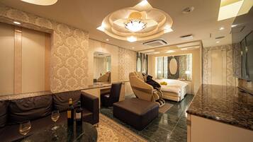 A modern hotel room with a sofa, ottoman, and a dining area.