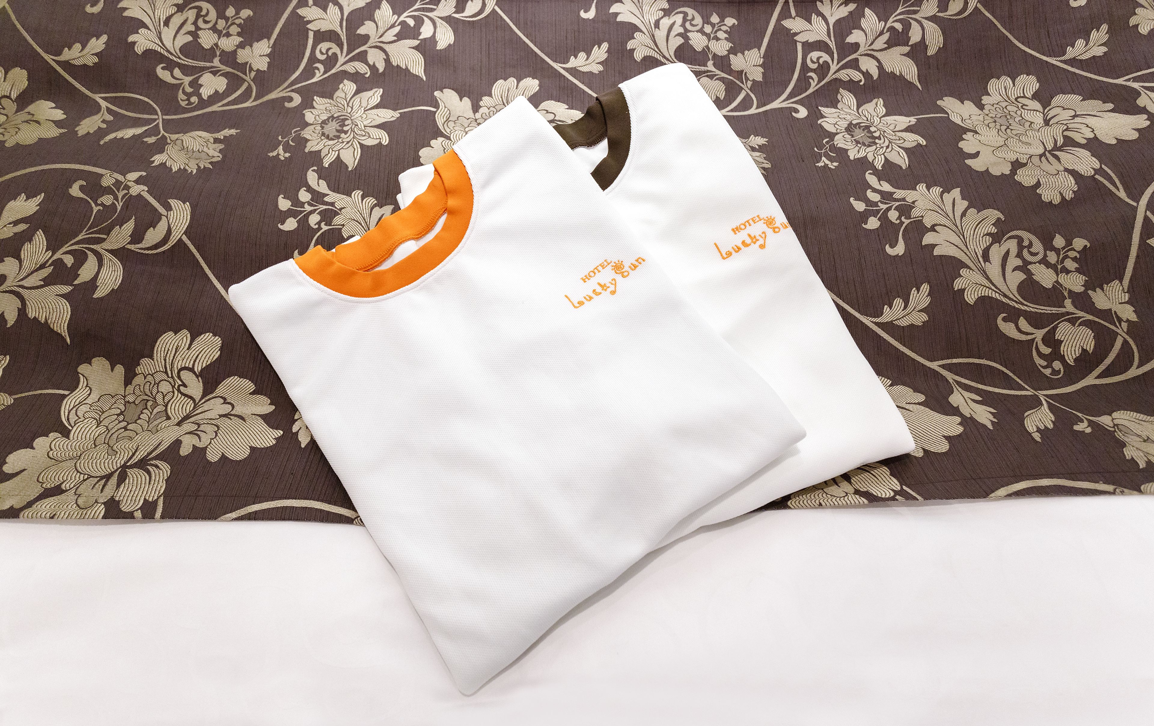 A white tote bag with orange accents and text on it, placed on a patterned fabric background.