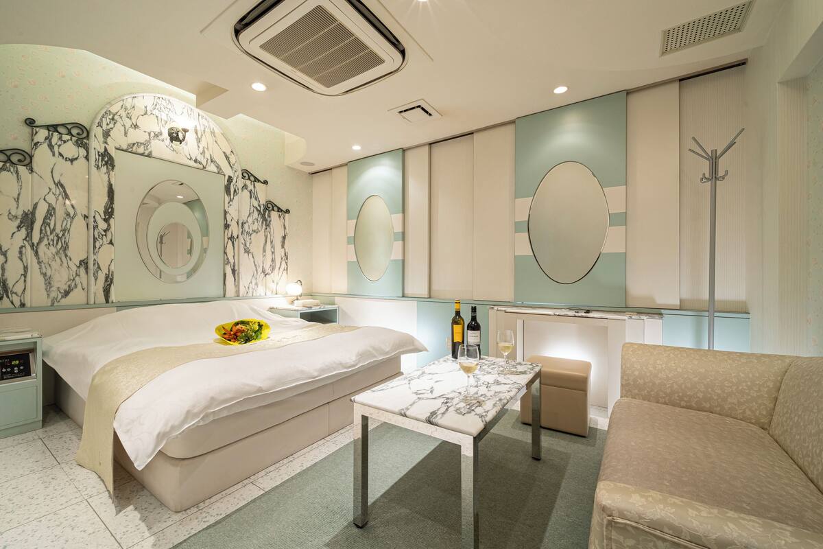 A modern hotel room with a bed, bedside table, a small table with a glass, and a sofa.