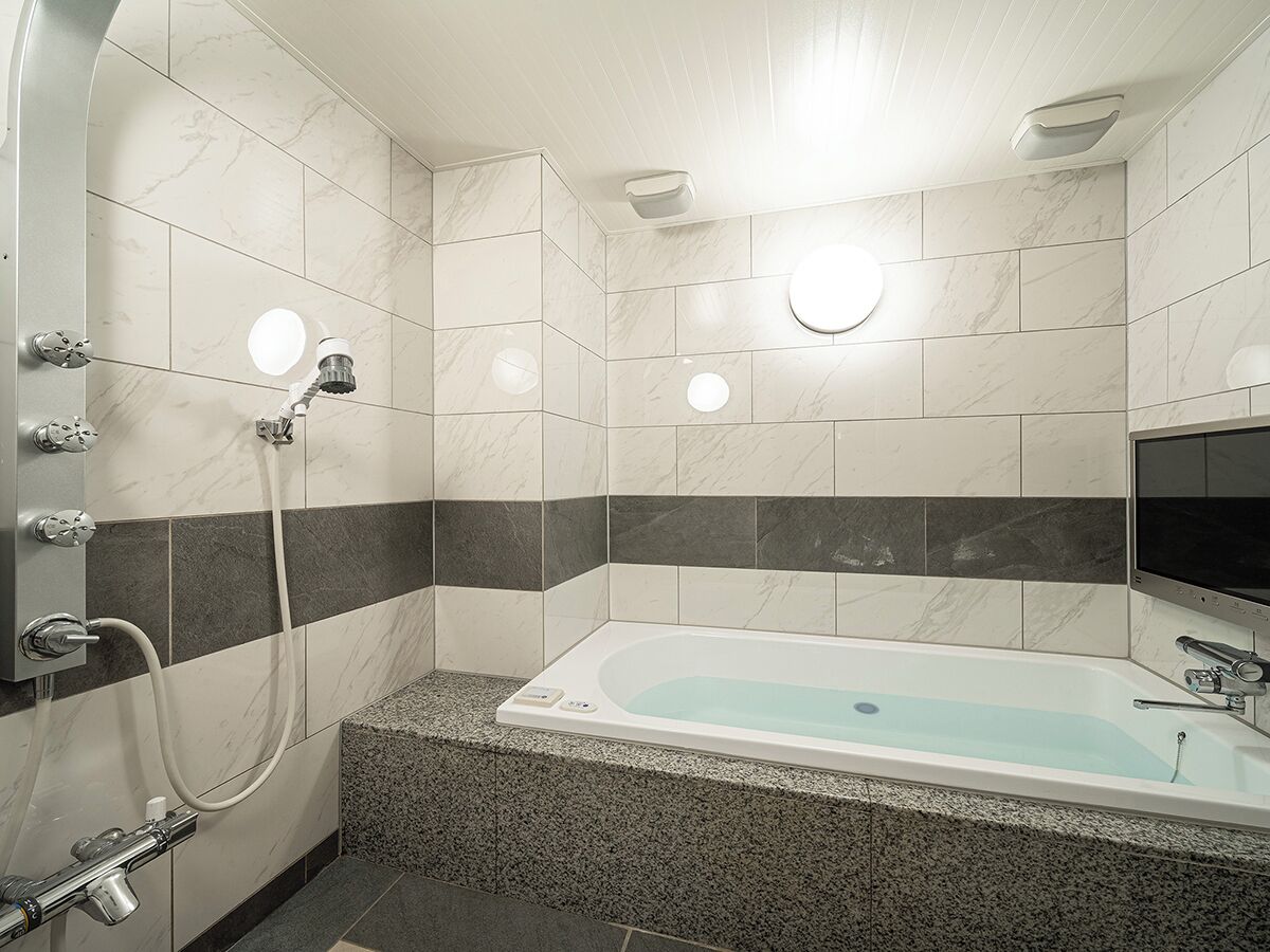 Een moderne badkamer met een vrijstaand bad, een handdouche en een wastafel op een muur bevestigd.