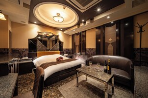 Quarto de hotel com cama, área de estar, mesa com garrafas de vinho e um cabideiro.