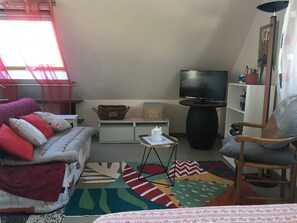 Una sala de estar acogedora con un sofá, una butaca, un televisor, una mesita y una alfombra colorida.