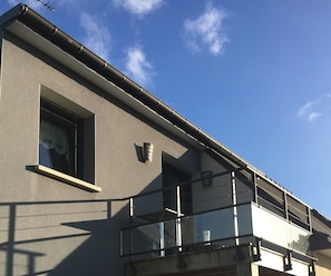 A building with a grey facade, a window with a curtain, and a balcony with a metal railing.