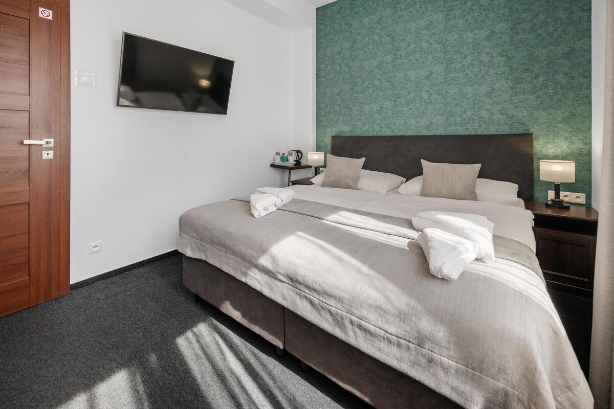 Una habitación de hotel con una cama grande, un televisor de pantalla plana montado en la pared, una mesita de noche con lámpara y una pared verde con textura.