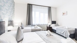 Habitación de hotel con dos camas, un ventanal con cortinas, un radiador y una mesita de noche con lámpara.