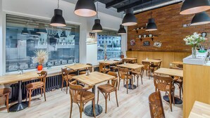 Interior de restaurante con mesas y sillas de madera, lámparas colgantes negras y pared de ladrillo.