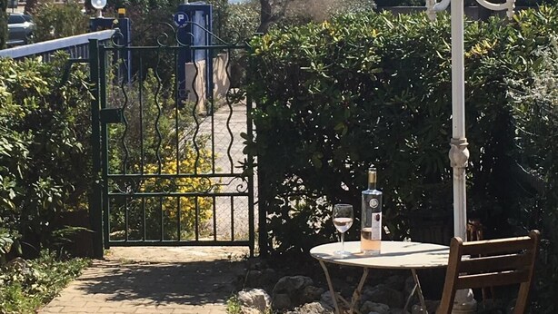 A paved pathway leading to a gated entrance with a table and chair, a street lamp, and a view of the sea.