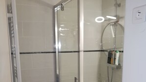 A glass-enclosed shower stall with a handheld showerhead, a towel rack, and a small shelf with toiletries.