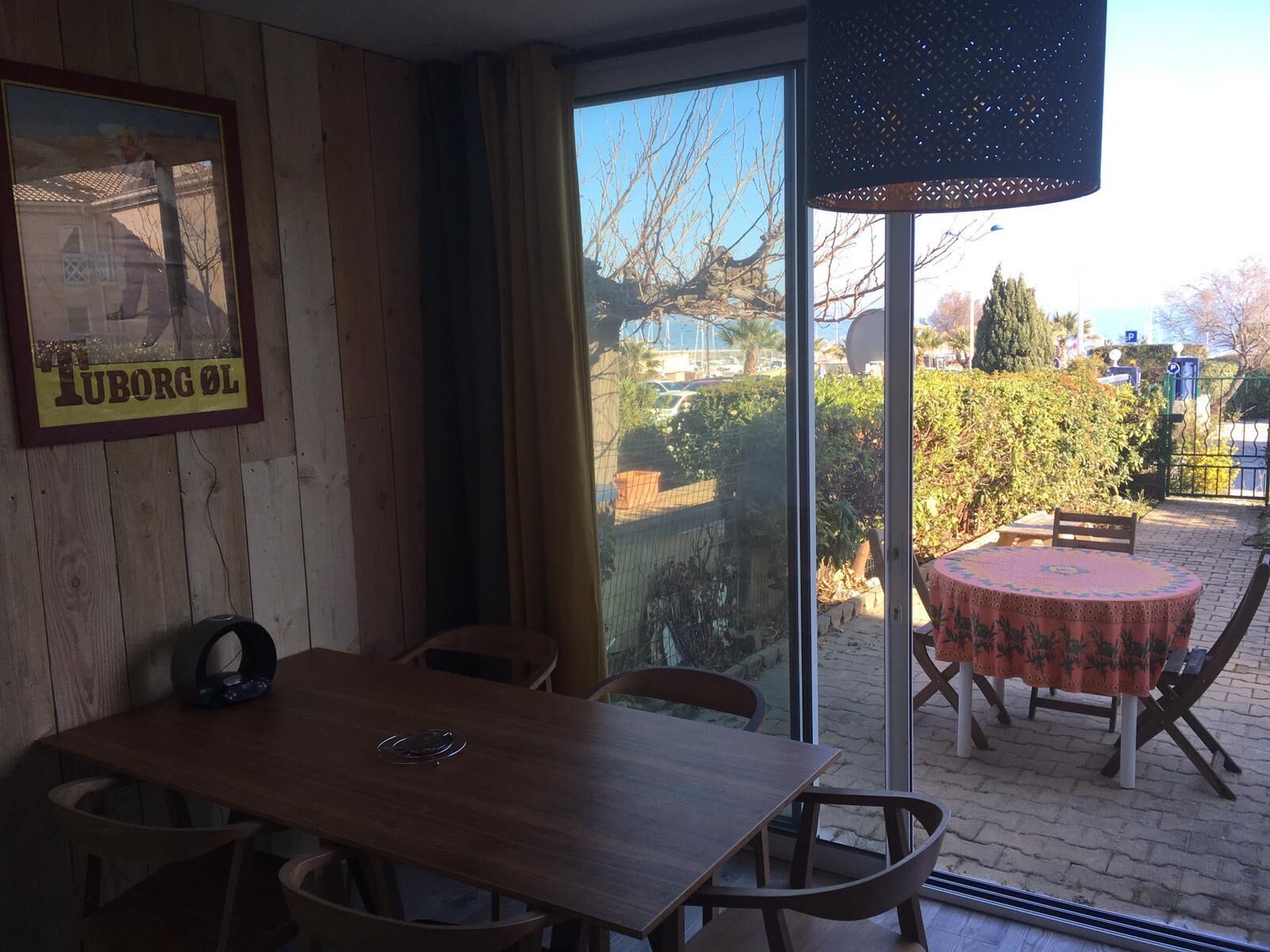 A dining area with a wooden table and chairs, a framed picture on the wall, and a view of the outside through a glass door.