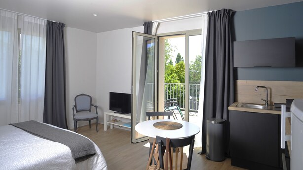 A modern hotel room with a bed, a TV, a dining table, and a balcony with a view of greenery. - Studio comfort in the heart of Jonzac (jonzac)