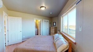 A bedroom with a bed, a dresser, a window with a view, and a door leading to another room. - Centurion: 3  BR, 2  BA House in Caplen, Sleeps 10 (Bolivar Peninsula)
