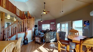 A spacious living area with a wooden staircase, a ceiling fan, and a view of the outside. - Centurion: 3  BR, 2  BA House in Caplen, Sleeps 10 (Bolivar Peninsula)