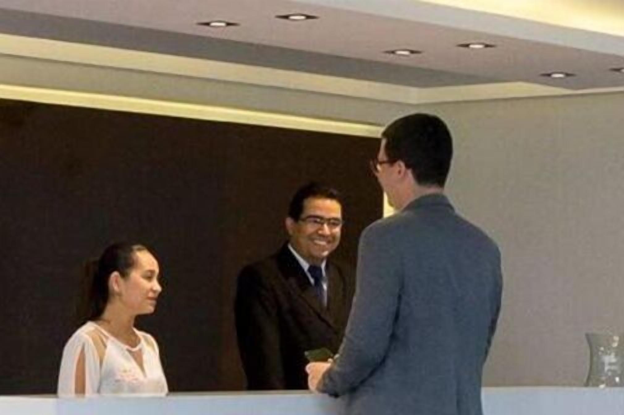 Un'area reception con una scrivania, un uomo in giacca che stringe la mano a una donna e un altro uomo in piedi accanto a loro.