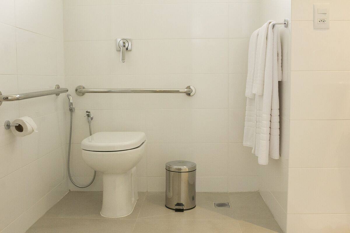 A small, modern bathroom with a toilet, bidet, and handrails.