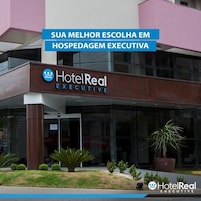 Um edifício HotelReal Executive com fachada de vidro moderna, um logotipo destacado e uma placa de identificação sobre a entrada.