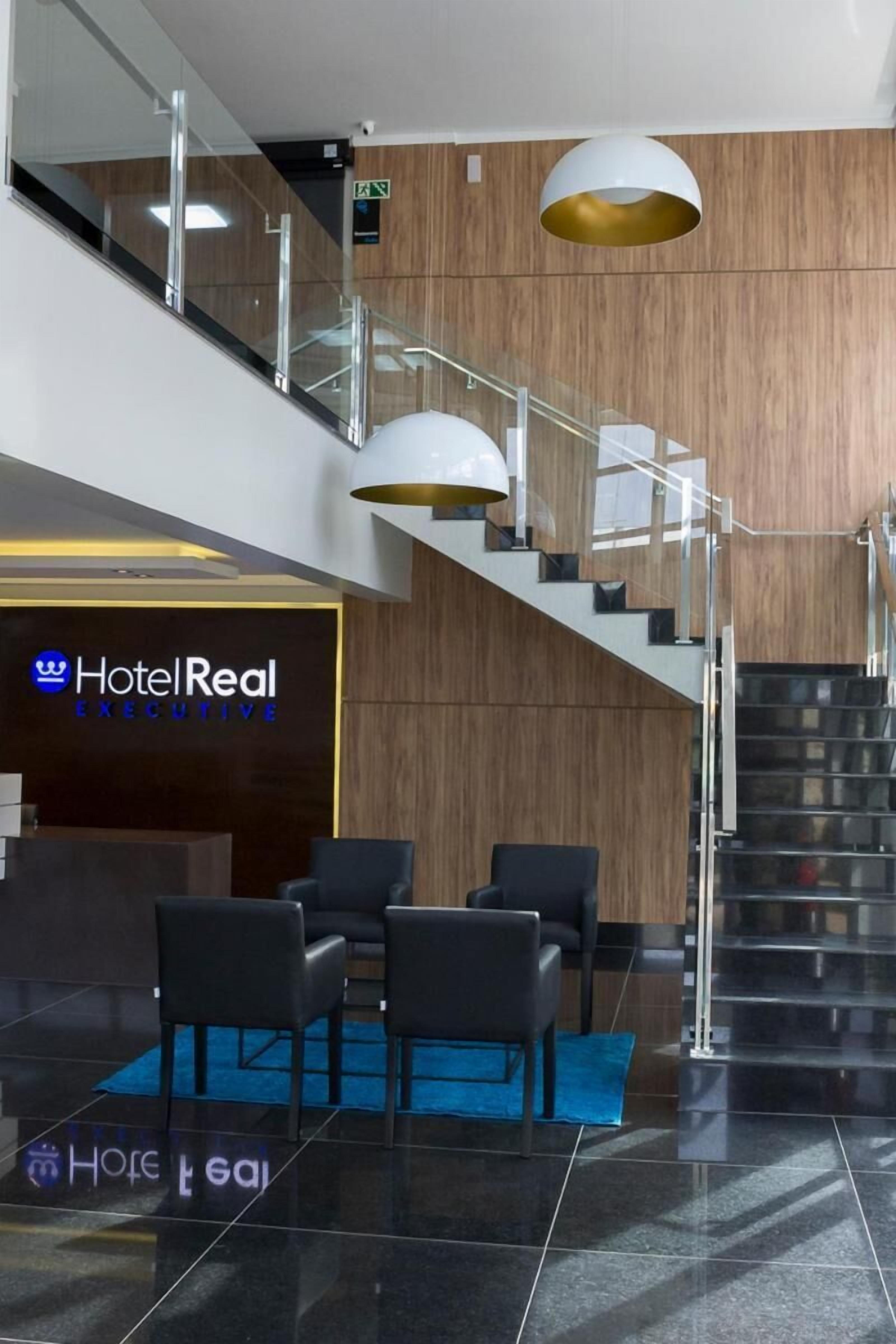 A hotel lobby with a reception desk, a staircase, and a seating area.