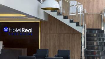 A hotel lobby with a reception desk, a staircase, and a seating area.