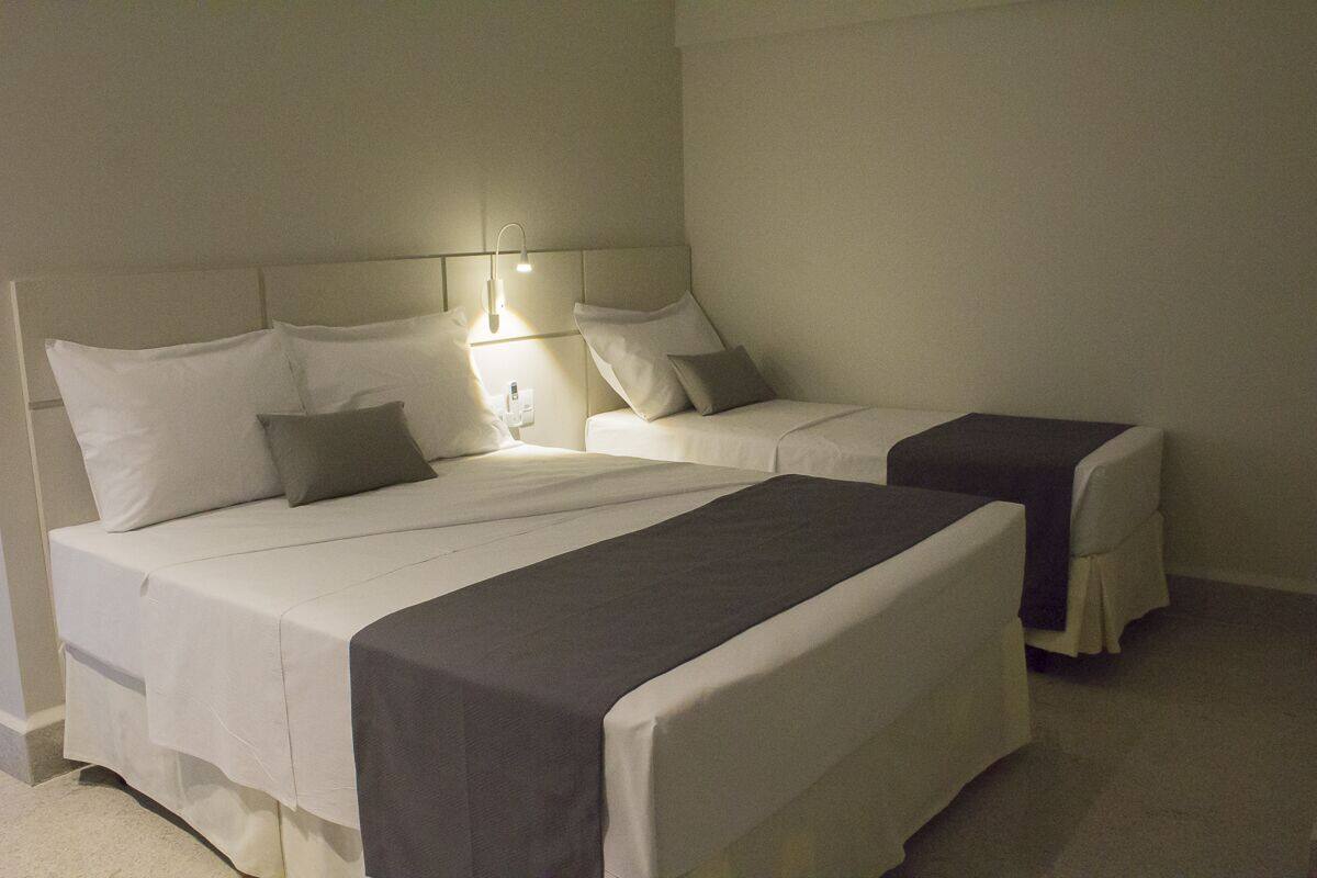A hotel room with two beds, each with white linens and pillows, a bedside table with a lamp, and a carpeted floor.