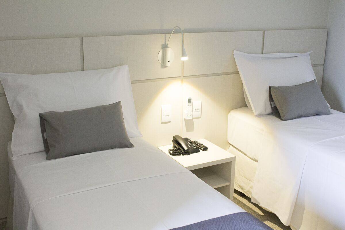 A hotel room with two beds, a bedside table with a phone, and a wall-mounted light fixture.