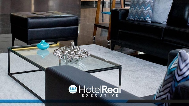 A modern hotel lobby with a reception desk, a staircase, and seating areas.