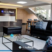 Um hall de hotel moderno com balcão de recepção, escadaria e áreas de estar.