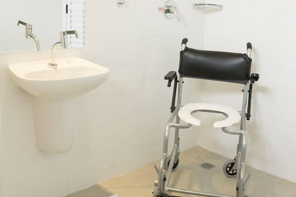 A bathroom with a white sink, a mirror, a shower, and a wheelchair-accessible toilet.