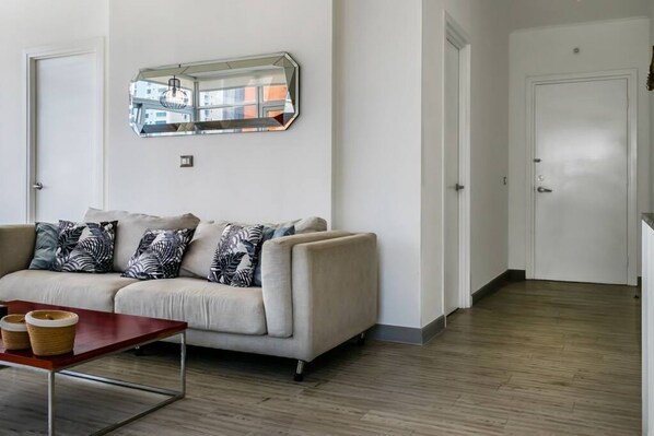 A living room with a beige sofa, patterned cushions, a wooden coffee table, and a large mirror on the wall. - Breath-taking City Center | PH Boutique Quartier Atlapa (Ciudad de Panamá)