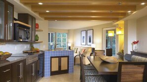 Una cocina moderna con una isla central, armarios oscuros y un comedor con mesa y sillas de madera.