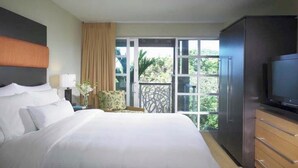 Habitación de hotel con una cama grande, televisor, armario y balcón con vistas a zonas verdes.