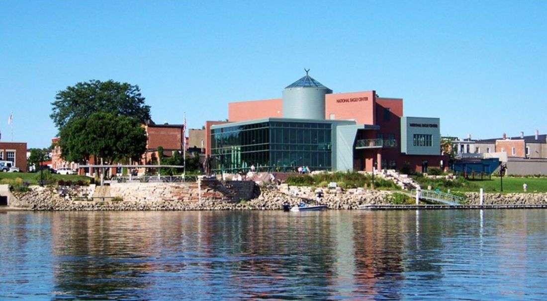 A modern building with a glass facade, a water body in front, and a stone pathway leading to it.