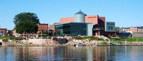 A modern building with a glass facade, a water body in front, and a stone pathway leading to it.