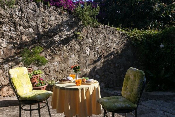 An outdoor seating area with two chairs and a table, surrounded by a rocky wall and greenery.