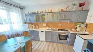 A compact kitchen with grey cabinets, a gas stove, a dishwasher, and a dining area with a table and chairs. - Holiday apartment with terrace and air conditioning (Novi Vinodolski)