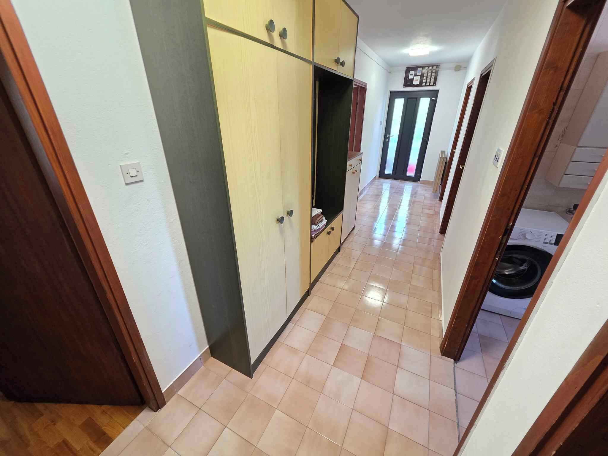 A hallway with a tiled floor, wooden doors, and a washing machine in the background.