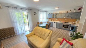 A living room with a yellow sofa, a dining table, and a kitchen area with grey cabinets and a stove. - Holiday apartment with terrace and air conditioning (Novi Vinodolski)