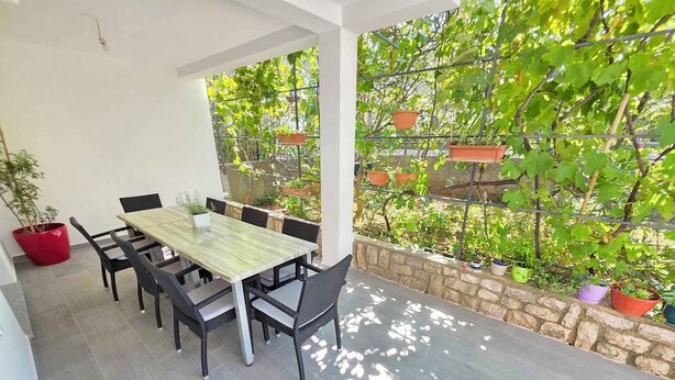A covered patio with a dining table and chairs, surrounded by potted plants and a stone wall. - Holiday apartment with terrace and air conditioning (Novi Vinodolski)