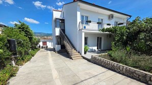 A two-story white building with a balcony, a staircase, and a stone wall. - Holiday apartment with terrace and air conditioning (Novi Vinodolski)