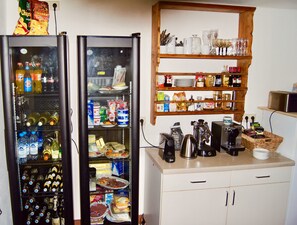 Two refrigerators stocked with beverages and snacks, a coffee maker, and a shelf with glassware and condiments. - Gästehaus Drachenfels (Oberstdorf)