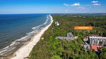 Vista aérea de una zona costera con playa, área boscosa y un edificio con la leyenda 'DWIE SOSNY'.