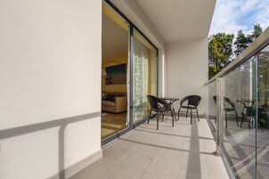 Ein Balkon mit Glastür, die in einen Wohnbereich führt, möbliert mit einer Couch und zwei Sesseln.