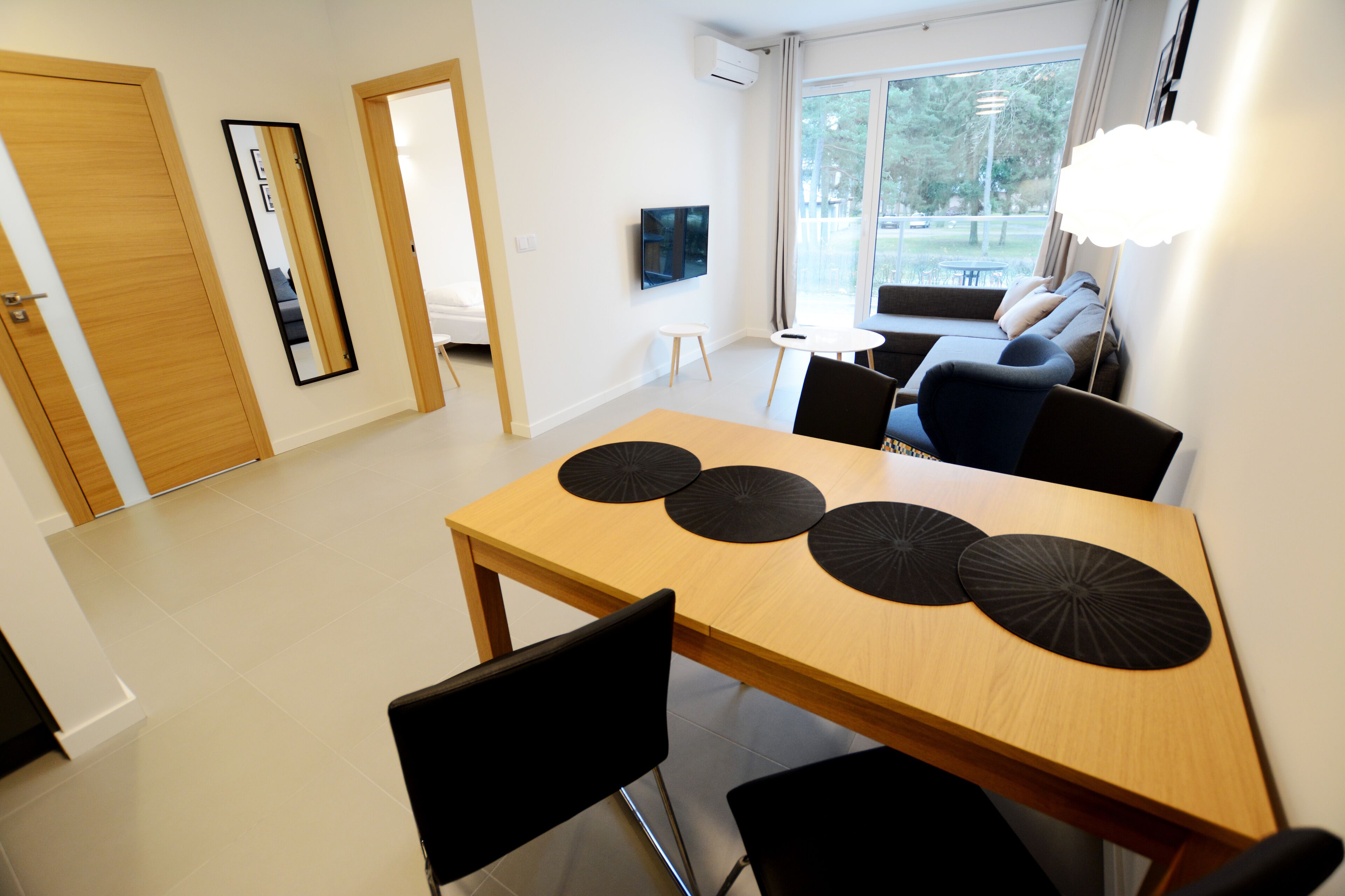 Un salon moderne avec un canapé, une table à manger agrémentée de sets de table noirs et un téléviseur fixé au mur.