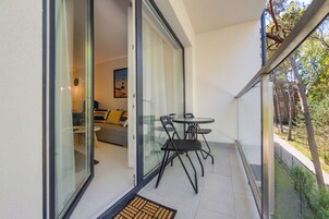 Un balcón con puerta de cristal que da a una sala de estar, una mesita y dos sillas.