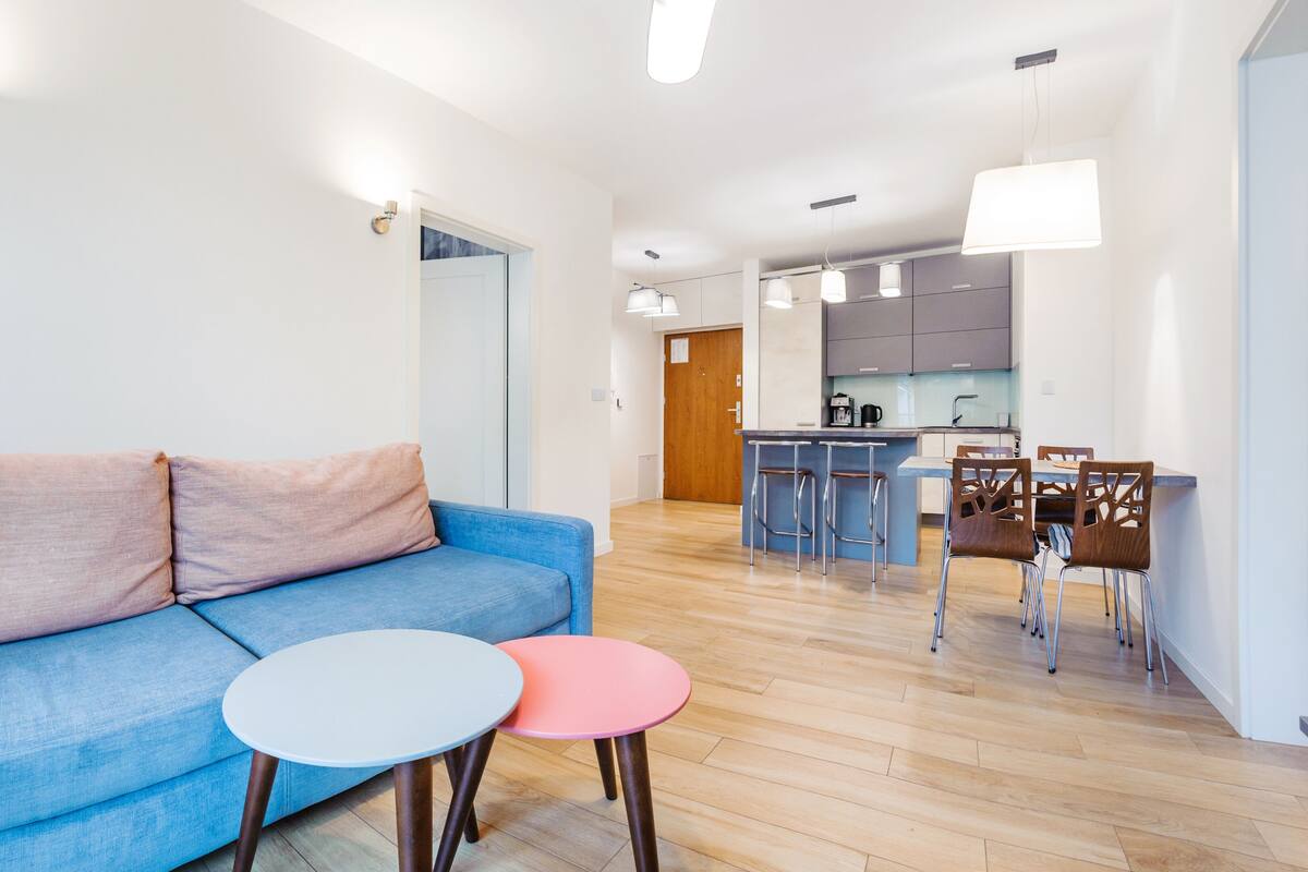 Un salon moderne avec un canapé bleu, deux petites tables rondes et un coin cuisine comprenant un bar et des tabourets.