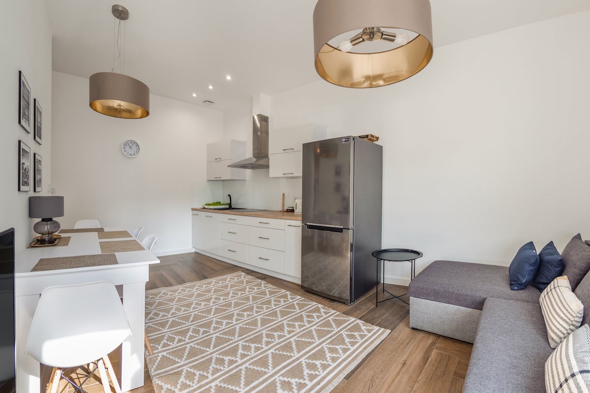 Une cuisine moderne avec des meubles blancs, un réfrigérateur en acier inoxydable et un coin repas comprenant une table et des chaises blanches.