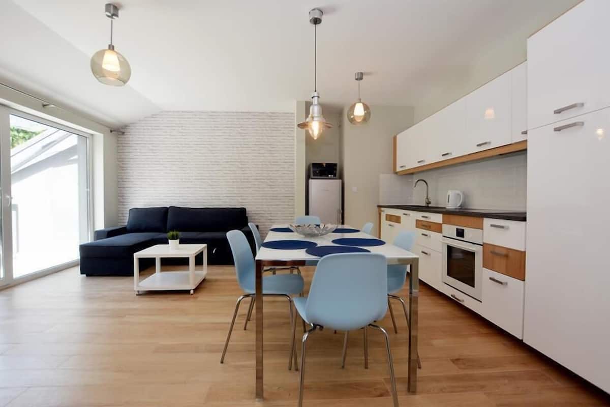Une cuisine moderne avec des meubles blancs, une table à manger entourée de chaises bleues et des luminaires suspendus.