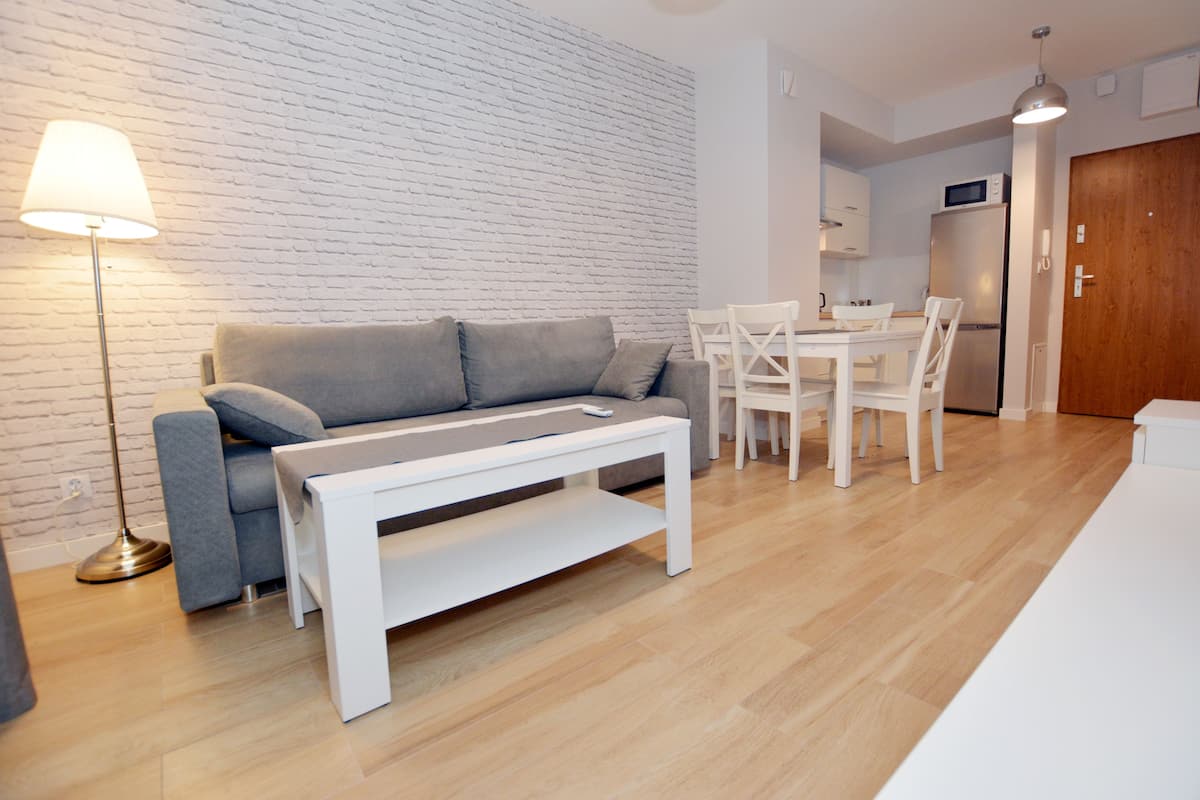 Un salon moderne avec un canapé gris, une table basse blanche et un coin repas comprenant des chaises et une table blanches.
