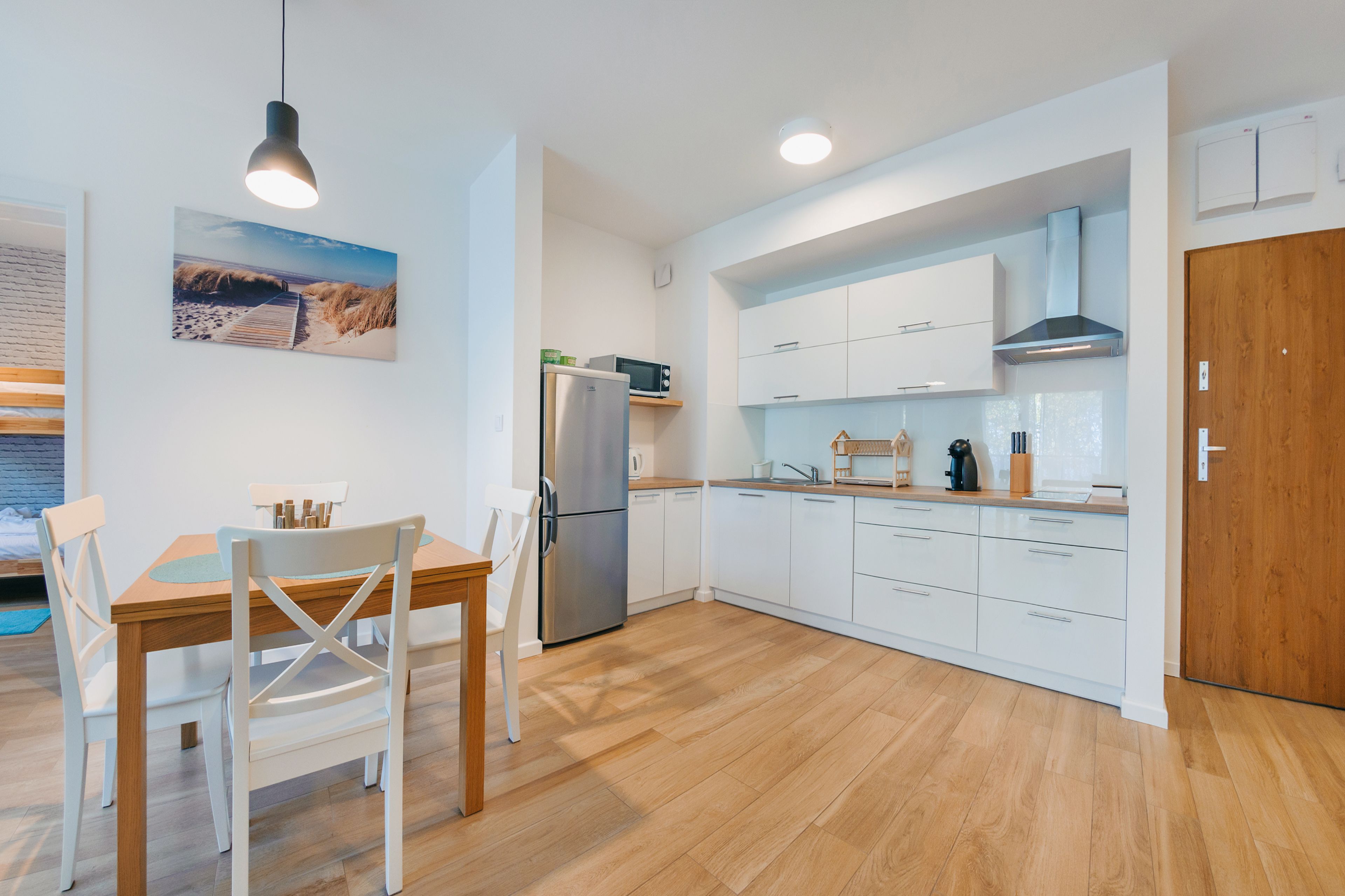 A modern kitchen with white cabinets, a stainless steel refrigerator, and a wooden dining table with white chairs.