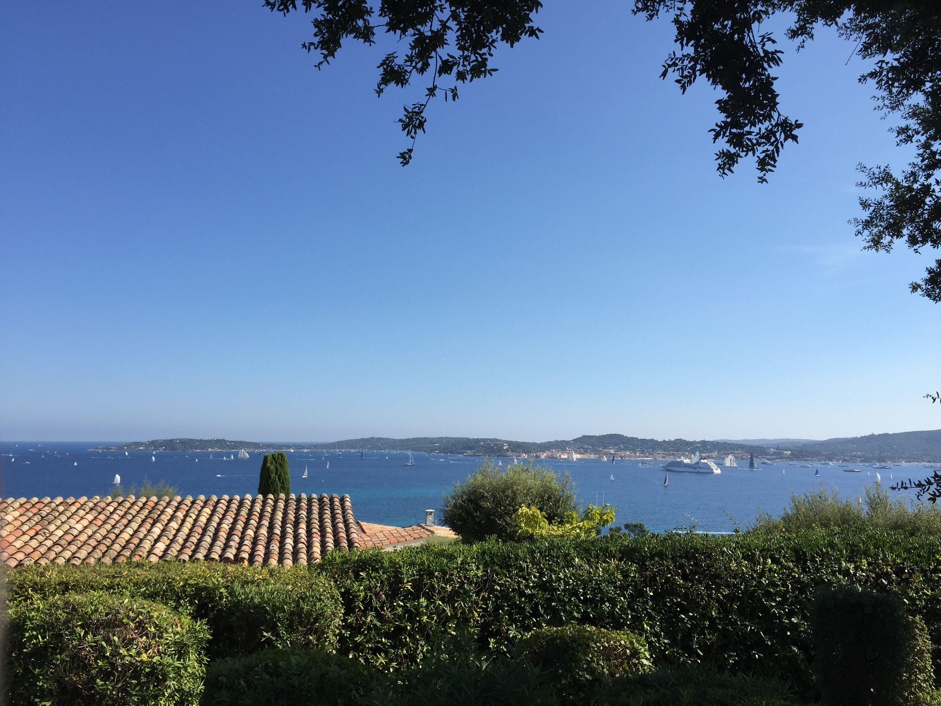 A coastal view with a clear sky, a tiled roof, and a body of water with boats.