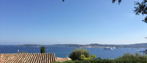 A coastal view with a clear sky, a tiled roof, and a body of water with boats.