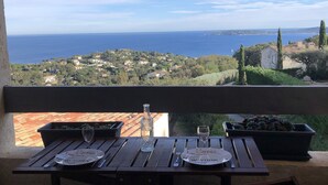A balcony with a table set for two, overlooking a coastal town and the sea.